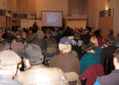 A meeting slide presentation in a full room of people